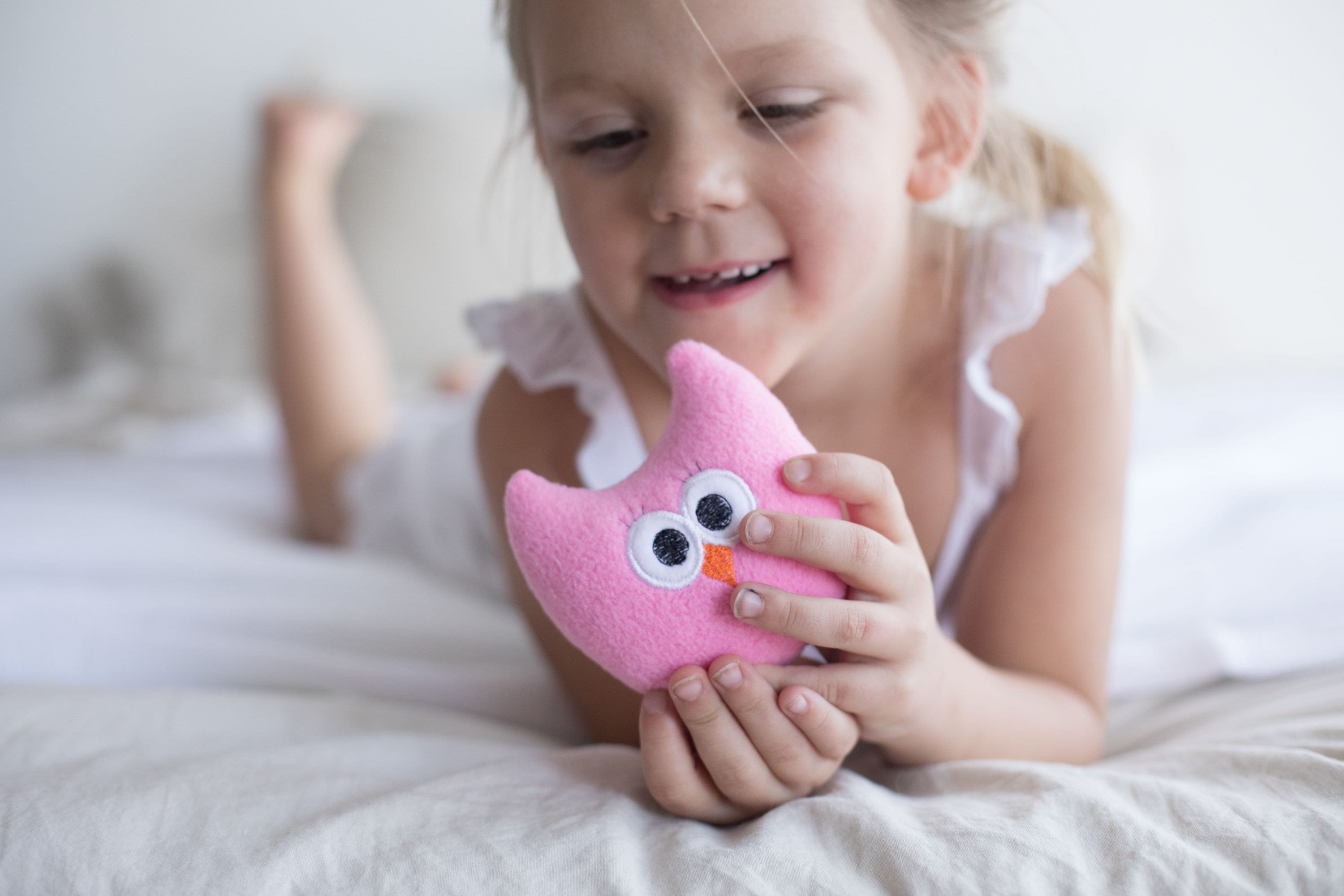 Child holding a pink owl plush toy on a bed